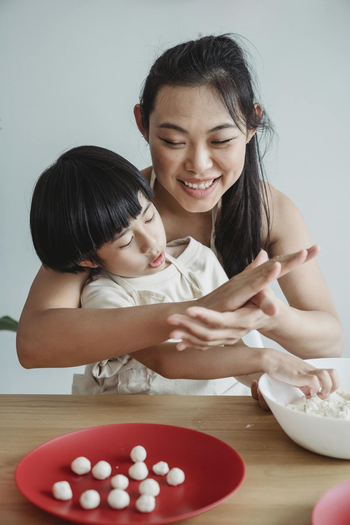 Mother teaching son to make dough. Smiling, they enjoy cooking together indoors.